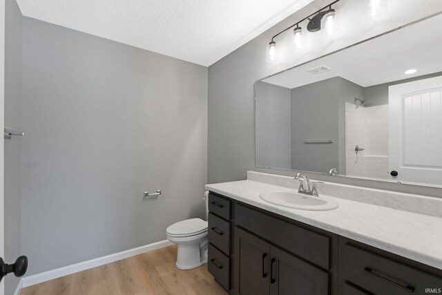 bathroom with walk in shower, a textured ceiling, toilet, vanity, and hardwood / wood-style flooring