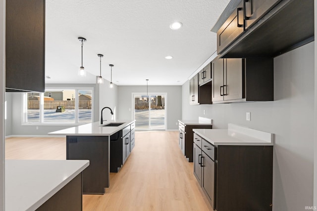 kitchen featuring sink, black dishwasher, pendant lighting, a kitchen island with sink, and light wood-type flooring