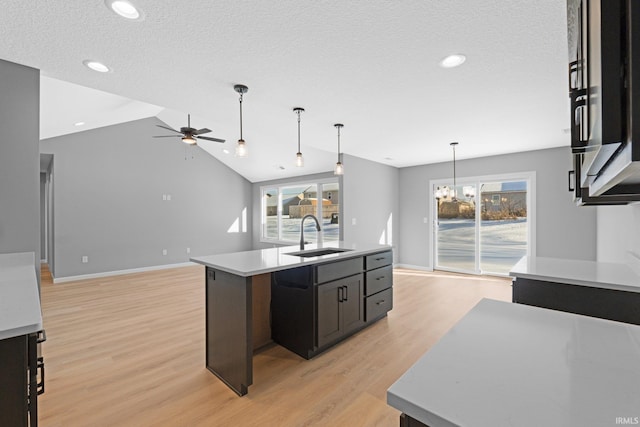 kitchen with sink, hanging light fixtures, light hardwood / wood-style flooring, a kitchen island with sink, and ceiling fan with notable chandelier