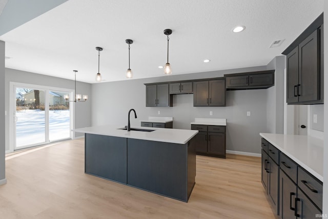 kitchen with sink, pendant lighting, a notable chandelier, light hardwood / wood-style floors, and an island with sink