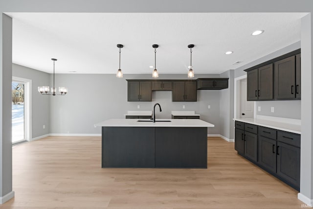 kitchen featuring decorative light fixtures, light hardwood / wood-style floors, sink, and a kitchen island with sink
