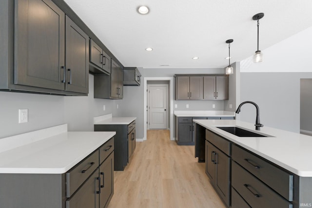 kitchen with decorative light fixtures, light wood-type flooring, an island with sink, and sink