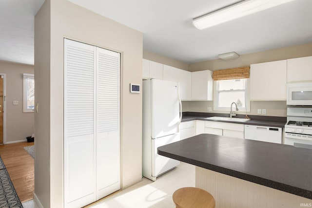 kitchen with light wood-type flooring, white appliances, sink, white cabinetry, and a breakfast bar area