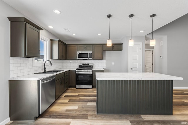 kitchen featuring backsplash, stainless steel appliances, sink, wood-type flooring, and hanging light fixtures