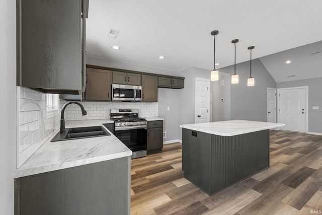 kitchen featuring sink, stainless steel appliances, vaulted ceiling, decorative light fixtures, and a kitchen island