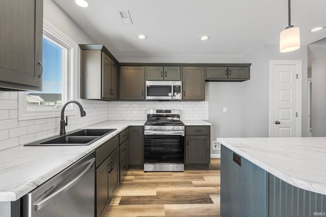 kitchen featuring appliances with stainless steel finishes, light wood-type flooring, tasteful backsplash, sink, and hanging light fixtures