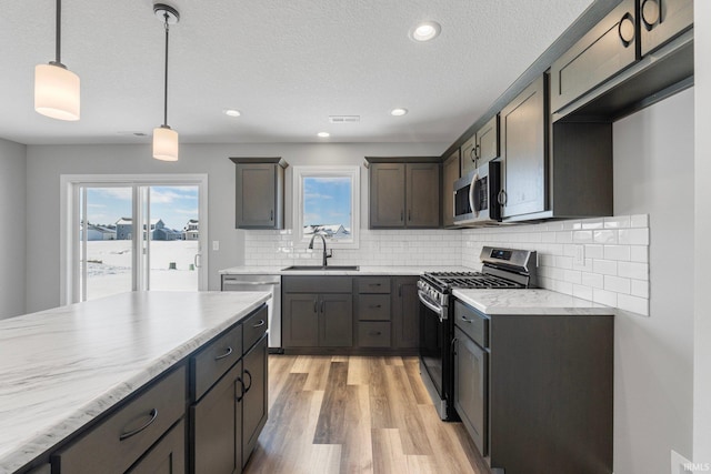 kitchen featuring sink, hanging light fixtures, stainless steel appliances, backsplash, and light hardwood / wood-style floors