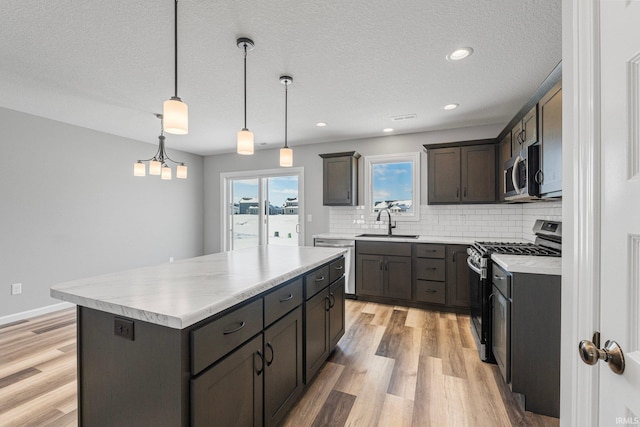 kitchen featuring stainless steel appliances, backsplash, light hardwood / wood-style floors, decorative light fixtures, and a kitchen island