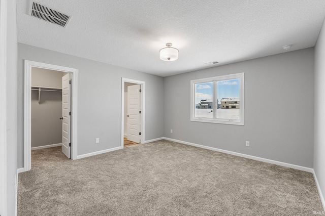 unfurnished bedroom with a textured ceiling, light colored carpet, a spacious closet, and a closet