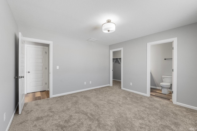 unfurnished bedroom featuring a walk in closet, ensuite bathroom, a textured ceiling, carpet floors, and a closet