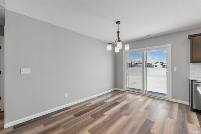 unfurnished dining area with a chandelier, a textured ceiling, and dark wood-type flooring