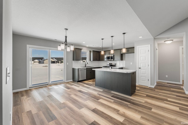 kitchen with appliances with stainless steel finishes, sink, pendant lighting, a center island, and lofted ceiling