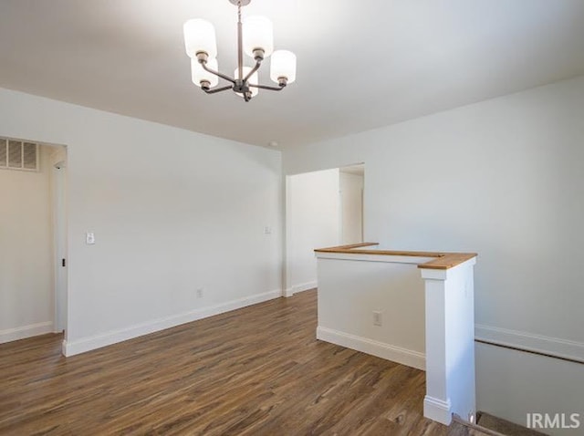 empty room with dark hardwood / wood-style flooring and a notable chandelier