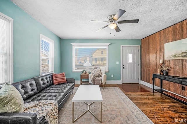 living room featuring a textured ceiling, dark wood-type flooring, ceiling fan, and wooden walls