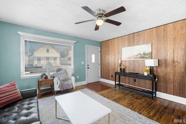 living room featuring hardwood / wood-style floors, ceiling fan, a textured ceiling, and wooden walls