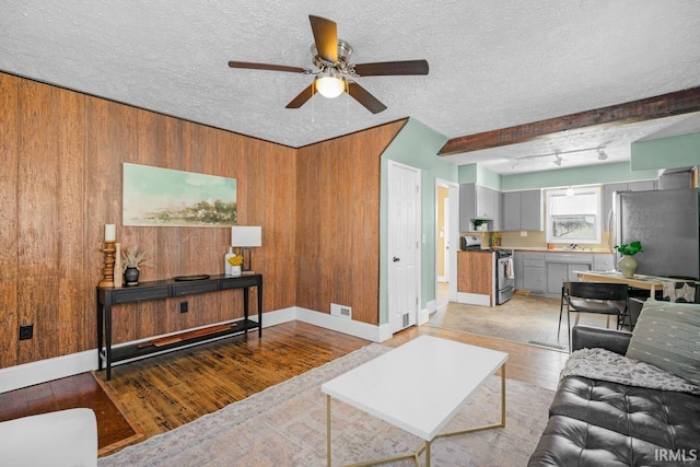 living room featuring light wood-type flooring, track lighting, a textured ceiling, ceiling fan, and wooden walls