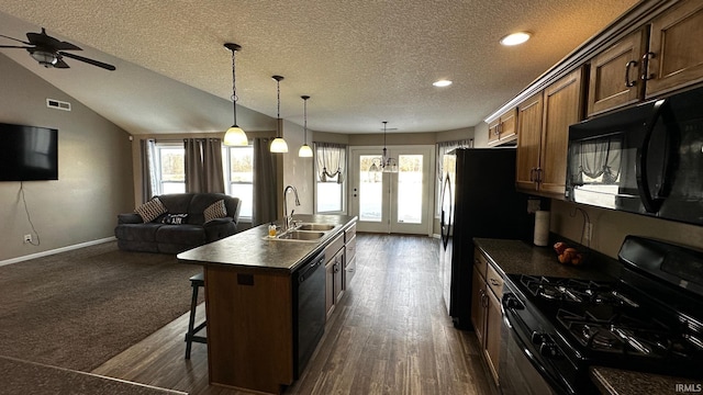 kitchen with a kitchen bar, a textured ceiling, black appliances, sink, and a center island with sink