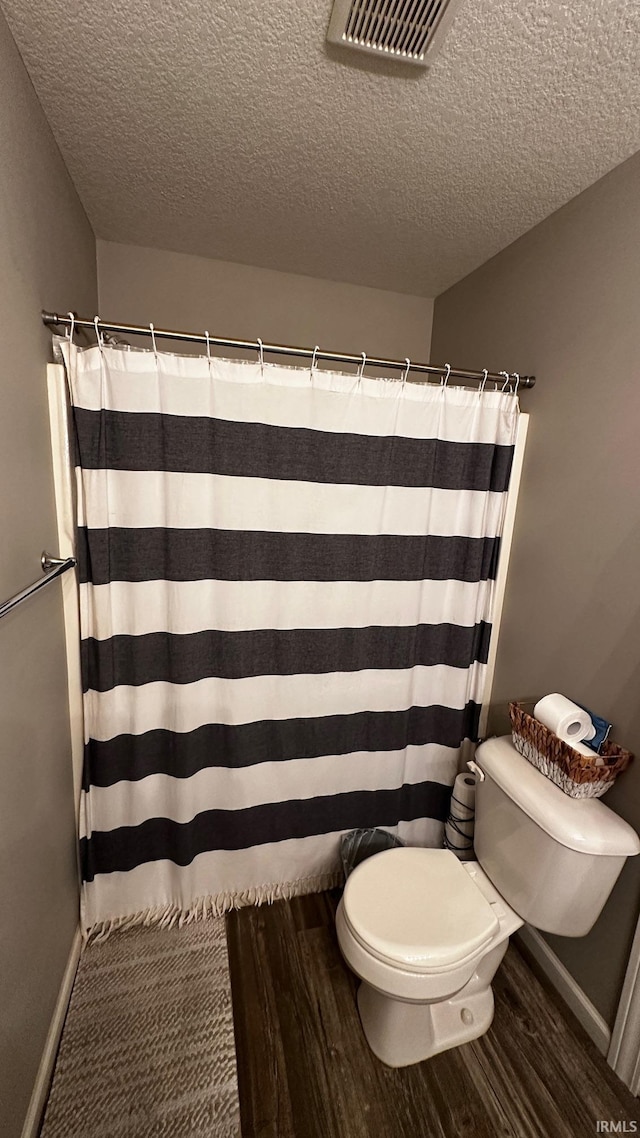 bathroom featuring curtained shower, toilet, wood-type flooring, and a textured ceiling