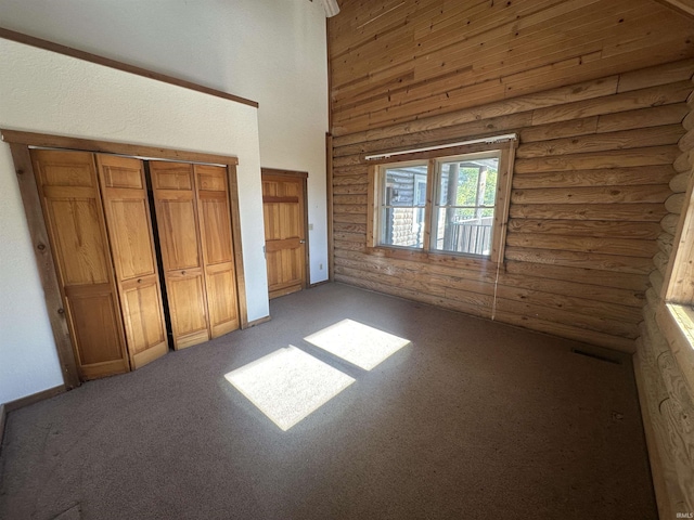 unfurnished bedroom featuring carpet flooring, a towering ceiling, a closet, and log walls