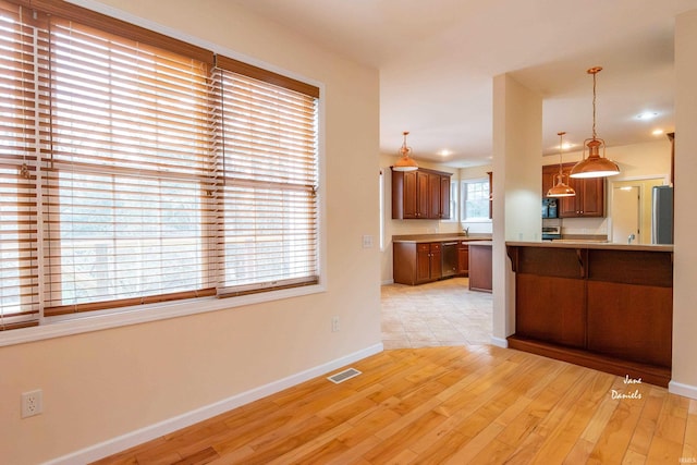 kitchen featuring decorative light fixtures, light wood-type flooring, kitchen peninsula, a wealth of natural light, and appliances with stainless steel finishes