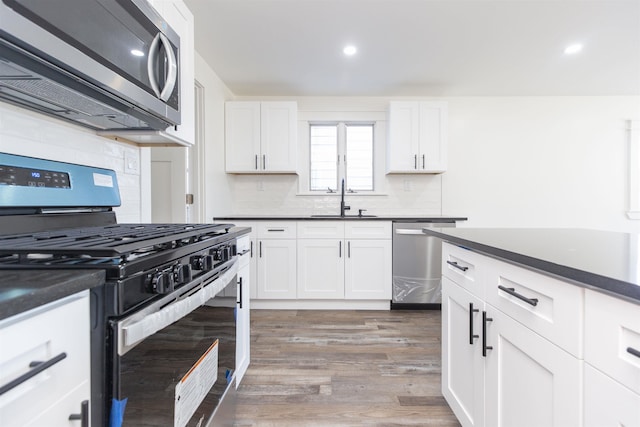 kitchen with appliances with stainless steel finishes, dark hardwood / wood-style flooring, white cabinetry, and sink