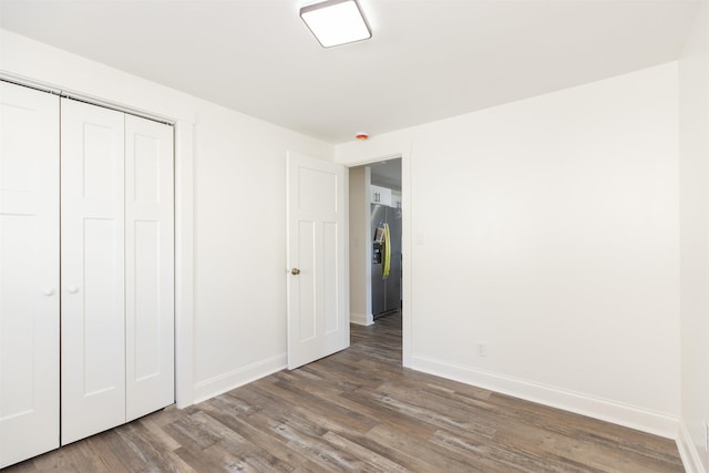 unfurnished bedroom with stainless steel fridge, a closet, and wood-type flooring