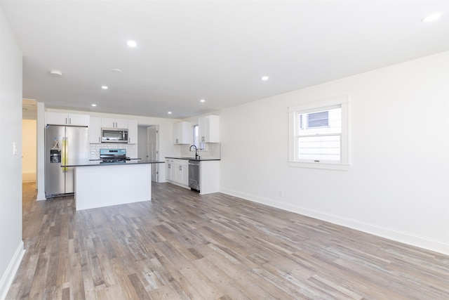 kitchen featuring white cabinetry, a center island, stainless steel appliances, backsplash, and light wood-type flooring