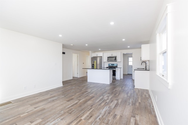 kitchen with appliances with stainless steel finishes, light wood-type flooring, sink, a center island, and white cabinetry