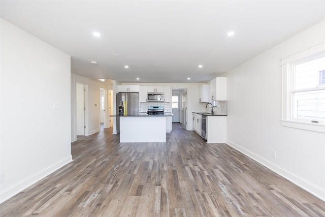 kitchen with a center island, hardwood / wood-style floors, decorative backsplash, white cabinets, and appliances with stainless steel finishes