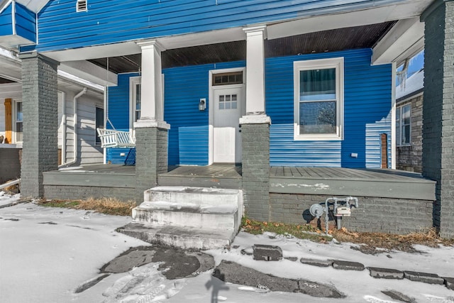 snow covered property entrance with covered porch