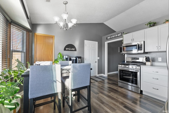 kitchen with white cabinetry, stainless steel appliances, an inviting chandelier, pendant lighting, and vaulted ceiling