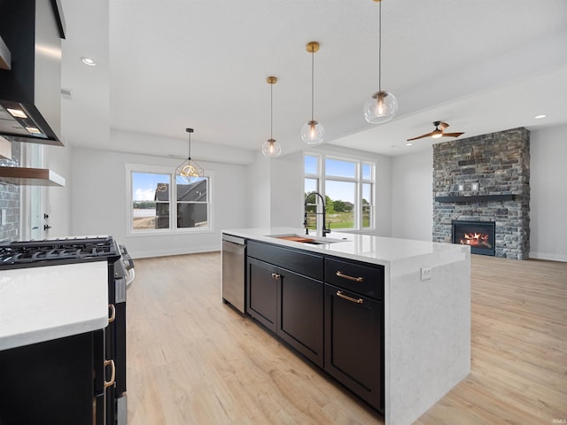 kitchen featuring stainless steel appliances, a kitchen island with sink, sink, a fireplace, and range hood