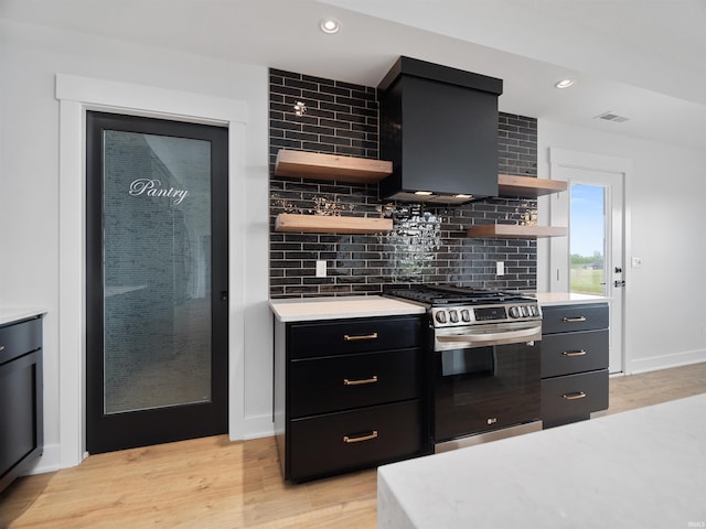 kitchen featuring light wood-type flooring, tasteful backsplash, stainless steel range with gas cooktop, and wall chimney range hood