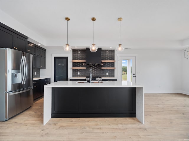 kitchen featuring tasteful backsplash, stainless steel fridge, light hardwood / wood-style floors, decorative light fixtures, and a kitchen island with sink