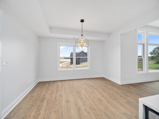 empty room with light wood-type flooring and a raised ceiling