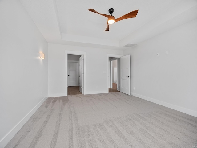 unfurnished bedroom with a tray ceiling, a spacious closet, ceiling fan, and light colored carpet