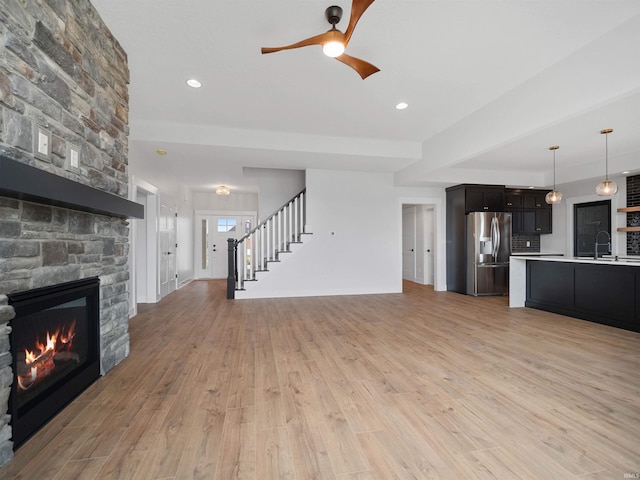 unfurnished living room featuring light wood-type flooring, a stone fireplace, ceiling fan, and sink