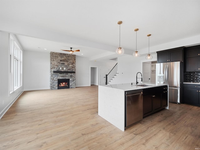 kitchen with a kitchen island with sink, hanging light fixtures, sink, a fireplace, and appliances with stainless steel finishes