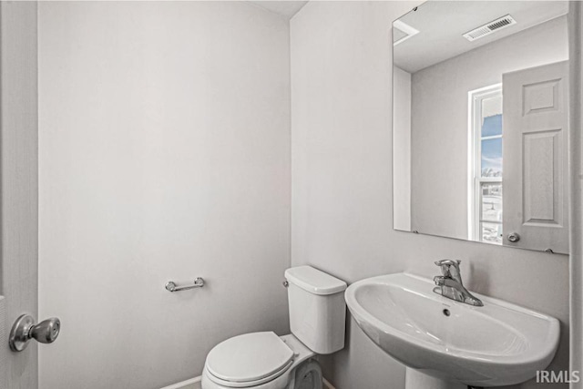 half bath with toilet, baseboards, visible vents, and a sink