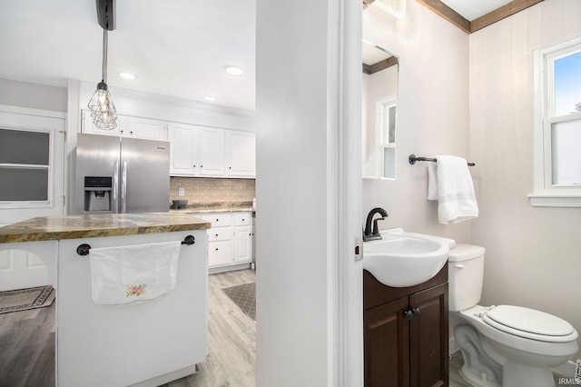 bathroom featuring backsplash, wood-type flooring, toilet, vanity, and ornamental molding