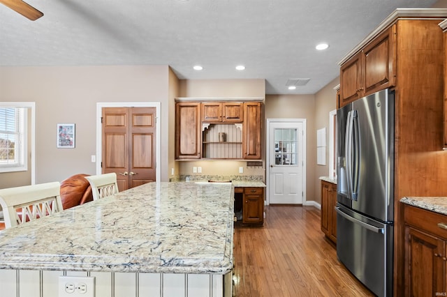 kitchen featuring a kitchen breakfast bar, light wood-type flooring, light stone countertops, stainless steel refrigerator with ice dispenser, and a kitchen island