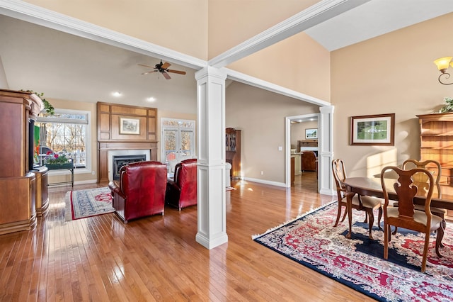 dining room featuring a fireplace, ornate columns, a towering ceiling, ceiling fan, and light wood-type flooring