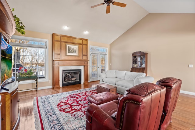 living room featuring ceiling fan, french doors, high vaulted ceiling, a fireplace, and light hardwood / wood-style flooring