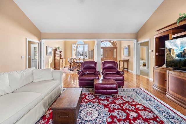 living room with light hardwood / wood-style flooring, an inviting chandelier, vaulted ceiling, and decorative columns