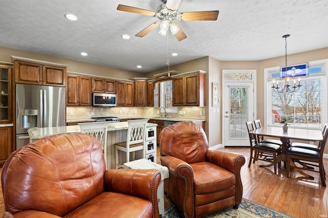 kitchen with stainless steel appliances, sink, light hardwood / wood-style flooring, decorative backsplash, and hanging light fixtures