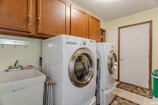 clothes washing area featuring sink, washing machine and dryer, a textured ceiling, and cabinets