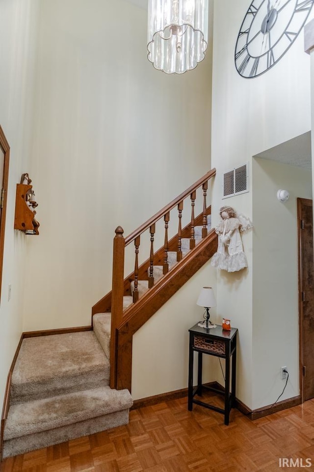 stairway featuring a high ceiling, an inviting chandelier, and parquet flooring