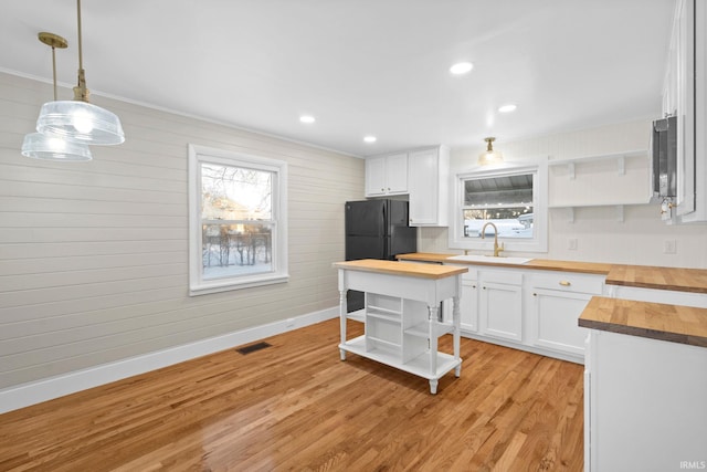 kitchen featuring wooden counters, hanging light fixtures, white cabinets, light hardwood / wood-style flooring, and sink