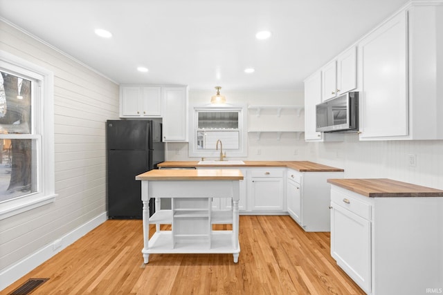 kitchen featuring black refrigerator, light wood-type flooring, wood counters, white cabinetry, and sink