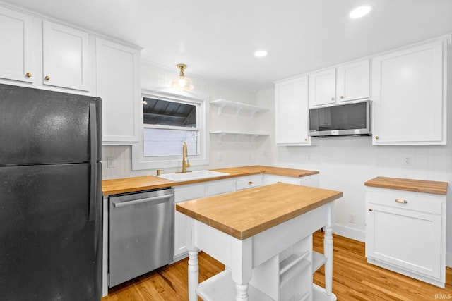 kitchen with stainless steel appliances, sink, white cabinetry, wood counters, and hanging light fixtures